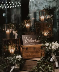 candles are lit in front of wooden boxes with welcome signs on them and greenery