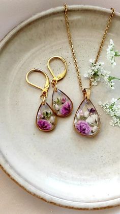 two necklaces with flowers on them sitting on a plate next to a flower bouquet