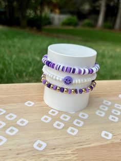 a stack of bracelets sitting on top of a wooden table next to a cup