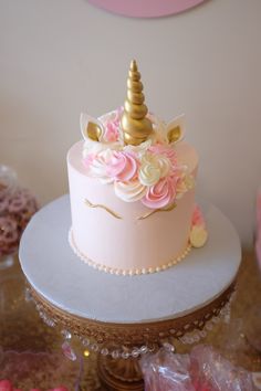 a pink and gold birthday cake with a unicorn topper on it's head