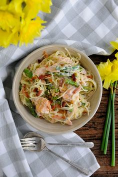 a white bowl filled with pasta and meat on top of a table next to yellow flowers