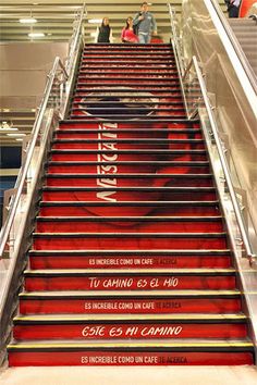 an escalator with red carpeted stairs and people walking up it in the background