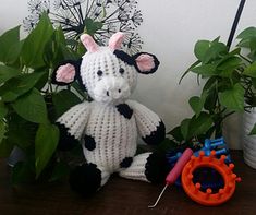 a crocheted cow sits next to some plants and a pair of scissors on a table