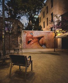 an empty park bench in front of a large painting on the side of a building