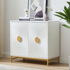 a white cabinet with two gold circles on the front and bottom, next to a potted plant