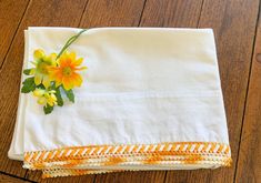 yellow flowers are placed on the edge of a white linen napkin with an orange border