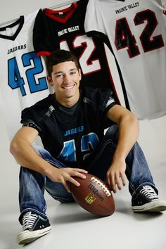 a young man sitting on the ground with a football in front of him and two jerseys behind him