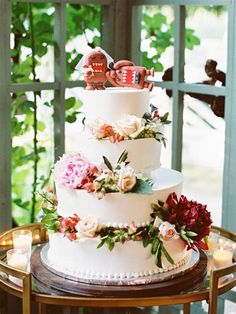 a three tiered wedding cake decorated with flowers and two figurines on top