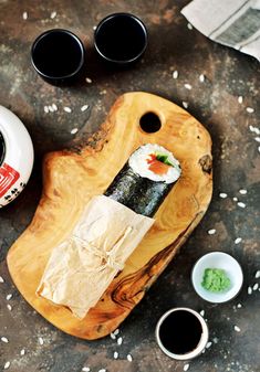 sushi on a wooden cutting board next to two small bowls