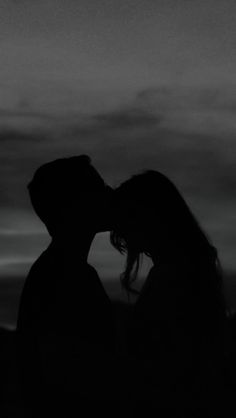 a man and woman kissing in the dark under a cloudy sky at sunset or dawn