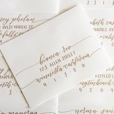 several envelopes with calligraphy written in gold ink on white paper, all lined up together