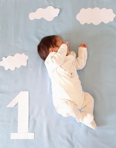 a baby laying on top of a blue blanket next to clouds and the number one