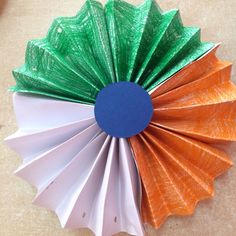 an orange, green and white paper flower with blue center sitting on top of a table