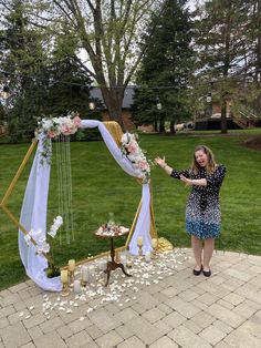 a woman standing next to a white and gold wedding arch