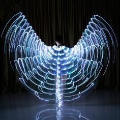 a person standing in front of a large light painting angel wings with lights on them