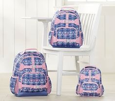 three pieces of pink and blue backpacks sitting next to a white chair