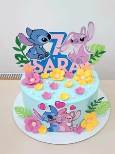 a blue cake with cartoon characters on top and flowers around the edges, sitting on a table