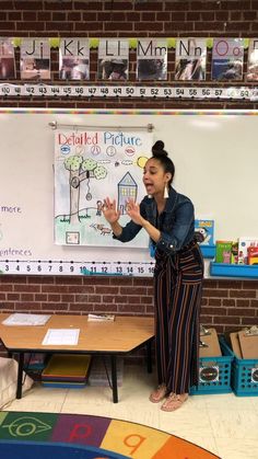 a woman standing in front of a whiteboard with writing on it and an open hand gesture