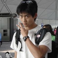 a young man is standing in an airport holding his hand up to his ear and looking at the camera