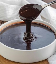 a spoon full of chocolate sauce on top of a white bowl filled with melted chocolate