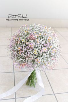 a bouquet of daisies and baby's breath tied to a white ribbon on a tiled floor