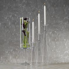 three tall glass vases with flowers and candles in them are on a table next to each other