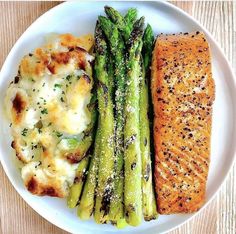 a white plate topped with asparagus, cheese and salmon next to broccoli