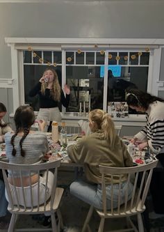 a group of people sitting around a table eating food and drinking beverages in front of a window