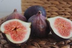 three figs sitting on top of a basket next to each other, one cut in half