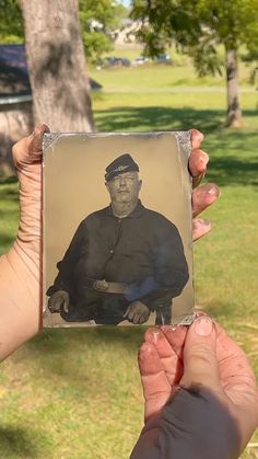 two hands holding up an old photo of a man in the middle of a park