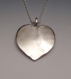 Heart Pendant made from a vintage Morgan silver dollar coin.  You can see the coin on the concave side and it can be worn either way.  This pendant comes on a sterling silver bead chain.  Please select length from the drop-down menu.To make one of these pieces, the face is sanded off on one side of a coin (except for those pieces with the coin image on both sides). Then using traditional hammering and forging techniques, the shape is formed, the designs are implanted, and the piece is domed with Silver Stamped Heart Pendant Jewelry, Sterling Silver Medallion Jewelry, Heart Dollar, Woodstock Ny, Silver Dollar Coin, Morgan Silver Dollar, Dollar Coin, Bead Chain, Silver Bead