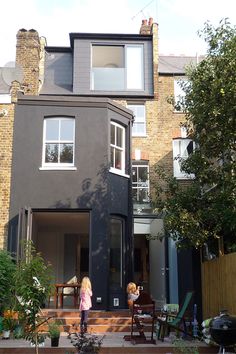 two children are standing in front of a black house with white windows and an upper level balcony