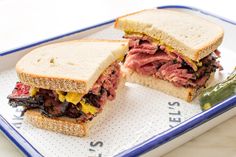 a roast beef sandwich cut in half on a blue and white platter with pickles