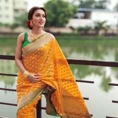 a woman in an orange and green sari sitting on a bridge next to water