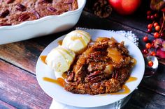 a white plate topped with fruit cobbler next to a bowl of ice cream and apples