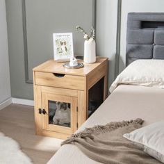 a bed with a wooden night stand next to it and a cat in the window