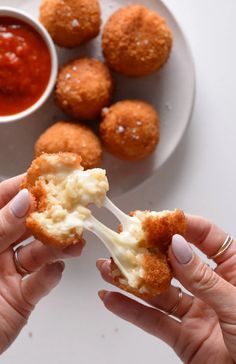 two hands holding food over a plate with dipping sauce on the side and other foods in the background