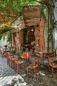 an outdoor cafe with tables and chairs on cobblestone pavement in front of brick building