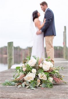 a bride and groom standing on a dock next to each other with flowers in the foreground