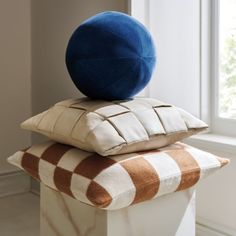 two pillows stacked on top of each other in front of a window with a blue pillow