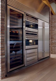 an empty kitchen with stainless steel appliances and brick walls, along with hardwood flooring