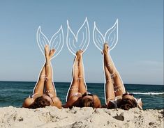 three women laying in the sand with their hands up above their heads, and two are upside down