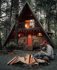 a man sitting on the ground next to a fire pit in front of a cabin