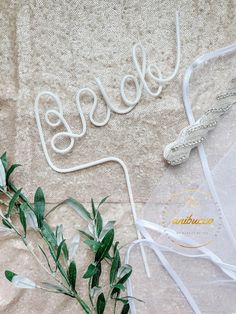 a white wire and some green leaves on a bed with the word love spelled in cursive writing