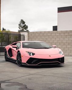 a pink sports car parked in front of a brick wall with black rims on it