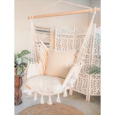 a white hanging chair next to a potted plant and wicker floor mat in a room