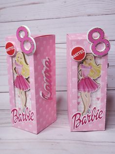 two pink boxes with barbie dolls in them on a white wooden surface, one has the number 8