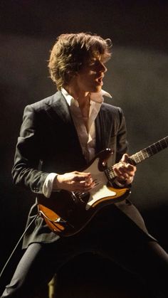 a man in a suit playing an electric guitar on stage with his legs spread out