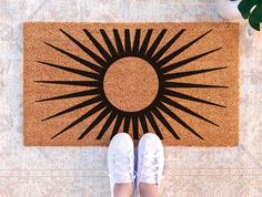 a person standing in front of a door mat with the sun design on it and white shoes