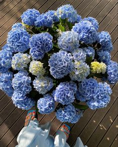 blue and white flowers in a vase on a wooden deck with someone's feet propped up